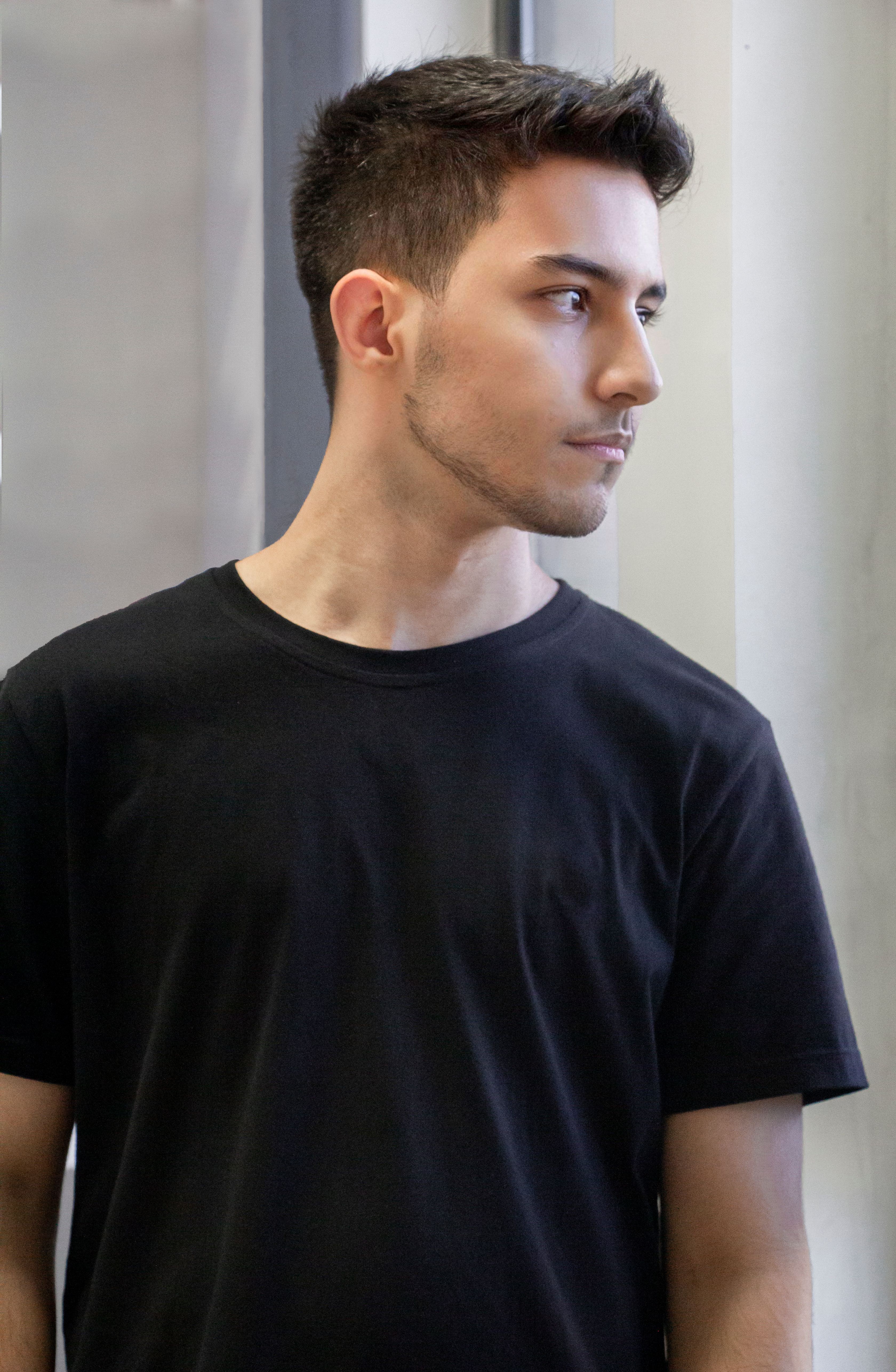 Portrait of a young man in a black t-shirt gazing thoughtfully out the window.