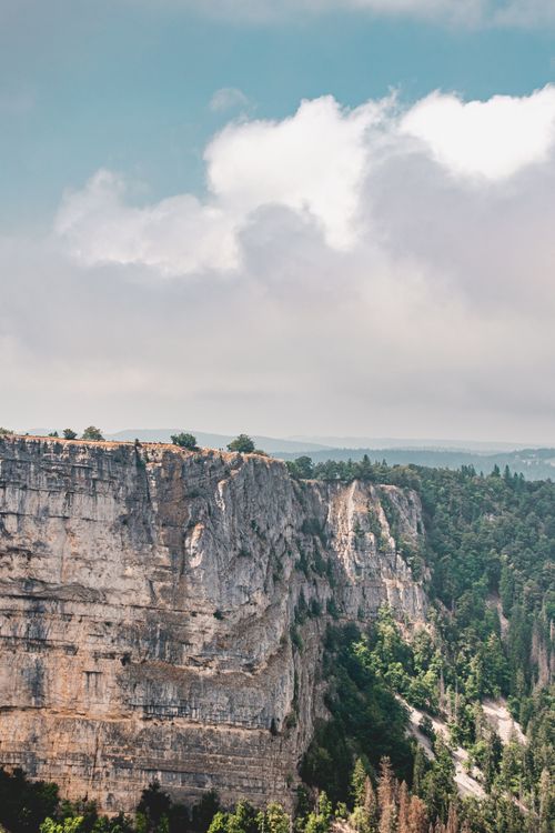 Free Majestic rocky cliff overlooking a dense forest with cloudy sky above, ideal for nature photography. Stock Photo
