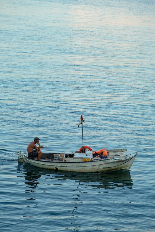 Free A lone fisherman navigates a small boat on a calm sea, with clear skies above. Stock Photo