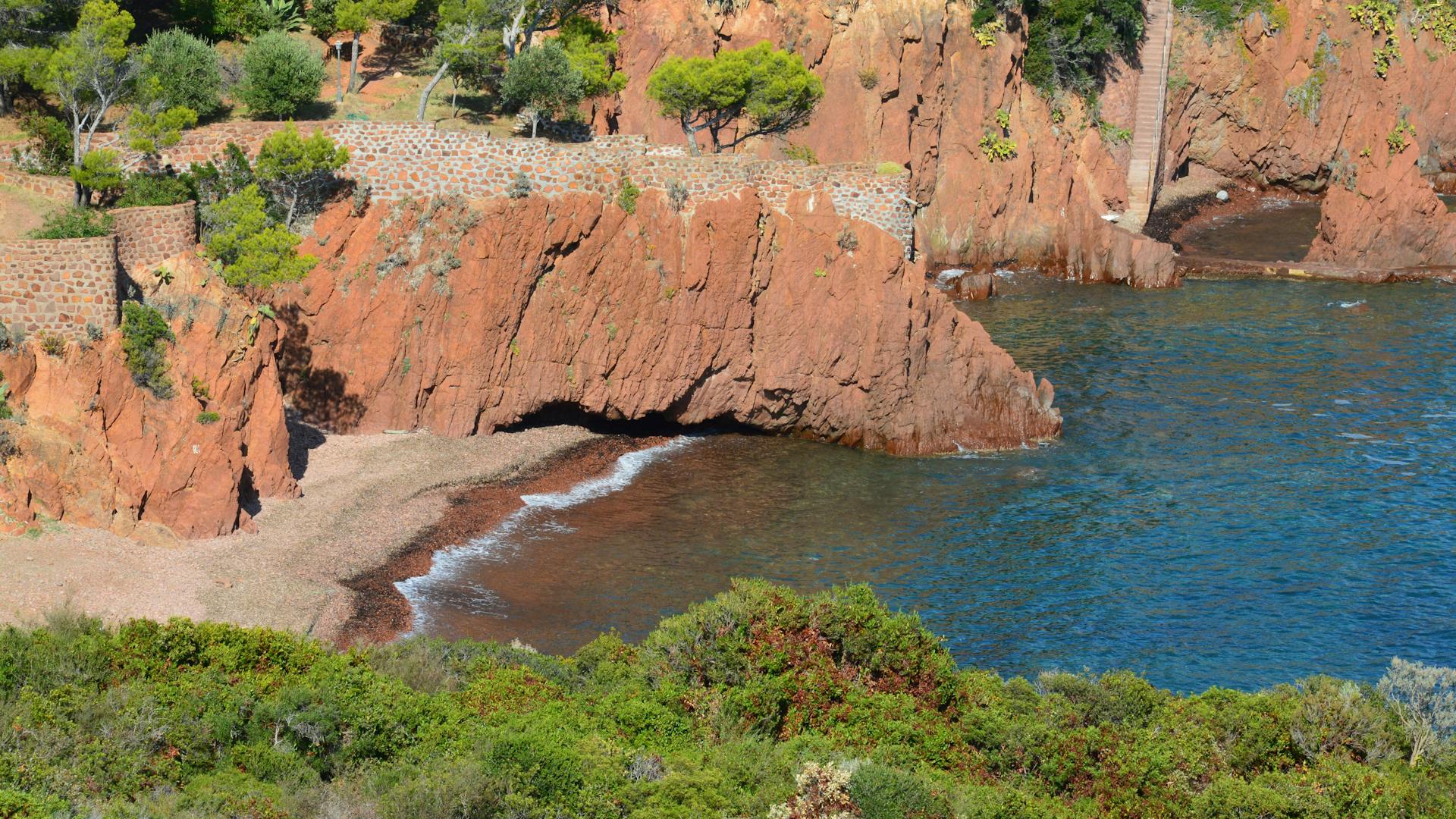 A stunning view of red coastal cliffs with lush greenery and calm azure waters, ideal for nature themes.