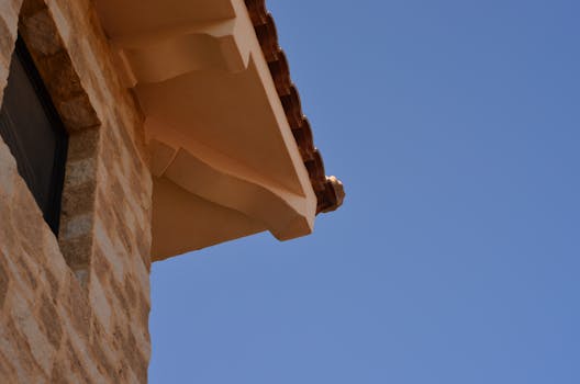 Low-angle view of a rustic stone building roof against a clear blue sky.