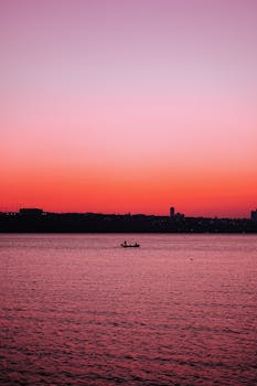 Silhouette of a boat against a vibrant pink and red sunset over calm waters.