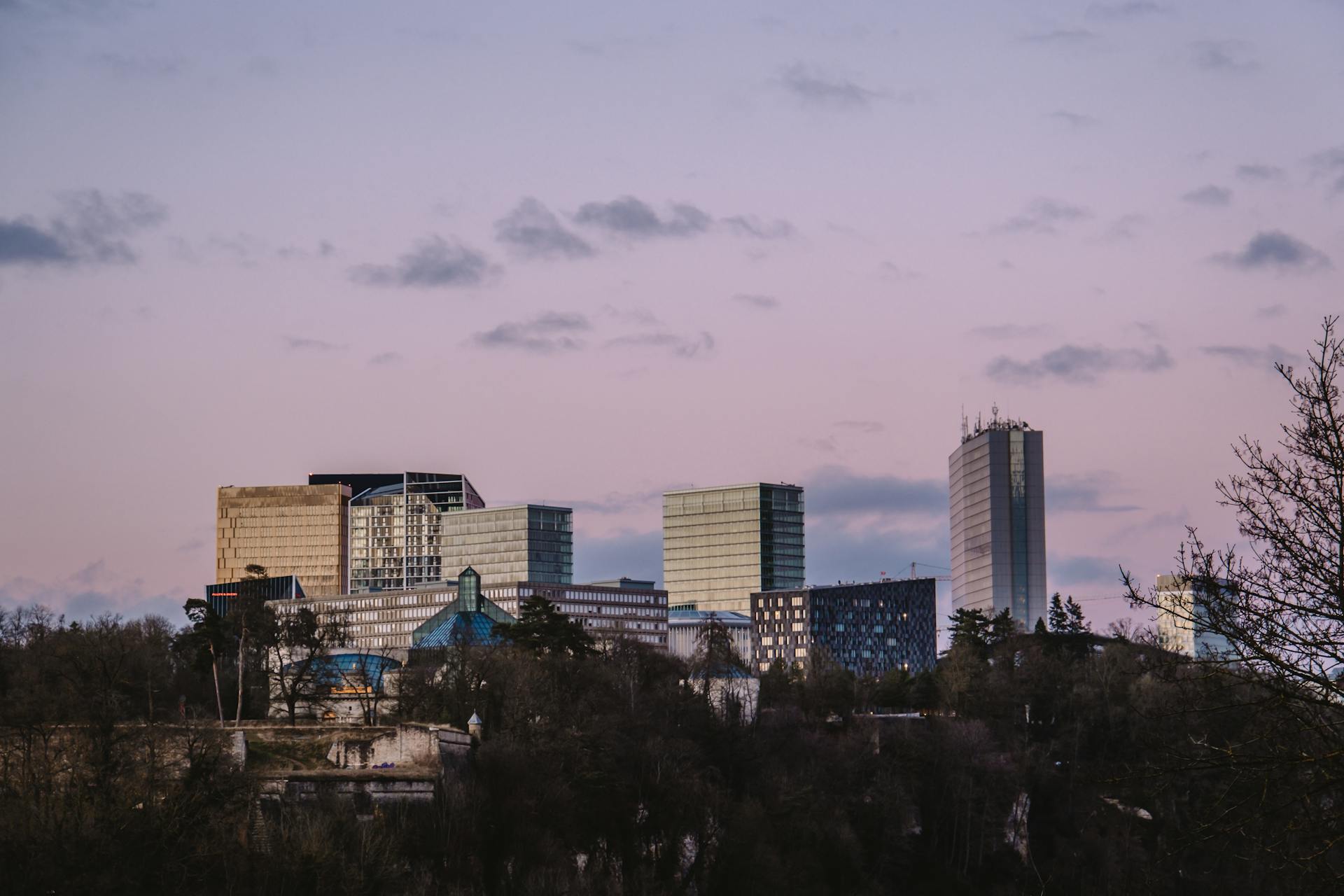 Luxembourg City skyline featuring modern skyscrapers under a soft pink sunset sky.