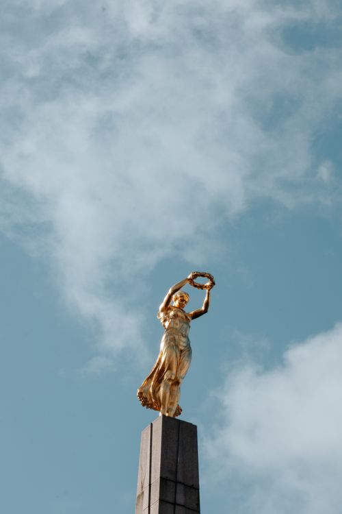 Free A golden statue atop a monument, set against a clear blue sky, symbolizing freedom. Stock Photo