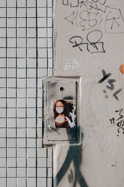 Urban graffiti of Mona Lisa with a face mask on a tiled and graffitied wall.