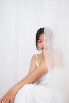 Portrait of an Asian woman in white dress behind a sheer curtain, exuding elegance and mystery.