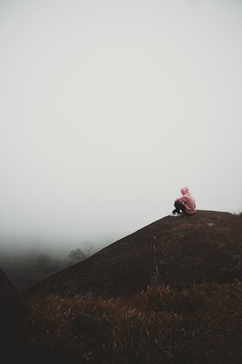 Person Sitting on Mountain Peak in Fog