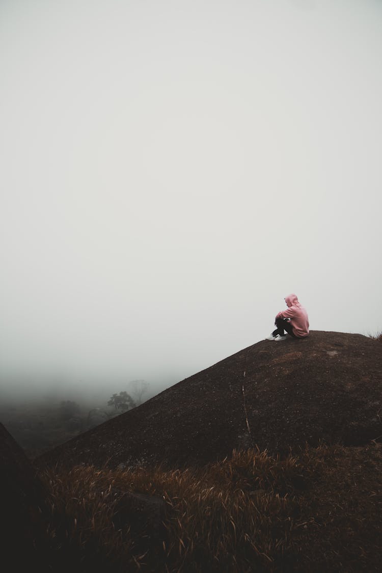 Person Sitting On Mountain Peak In Fog