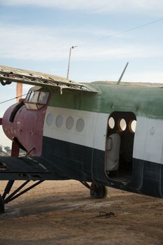 Close-up of a vintage aircraft on a desert runway, showcasing its weathered metal body and open door.