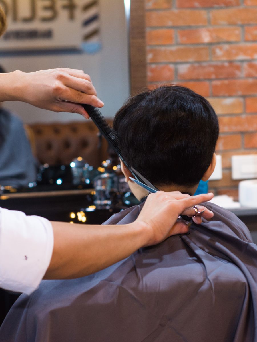 Barbeiro cortando o cabelo de um cliente com tesoura e pente