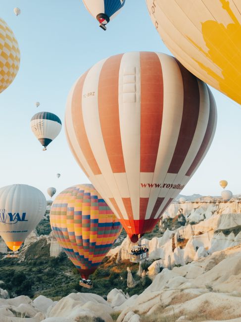 Colorful hot air balloons soar over Cappadocia's unique rock formations under a clear blue sky.
