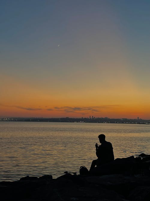 Silhouette of Person Sitting Beside the Sea during Sunset