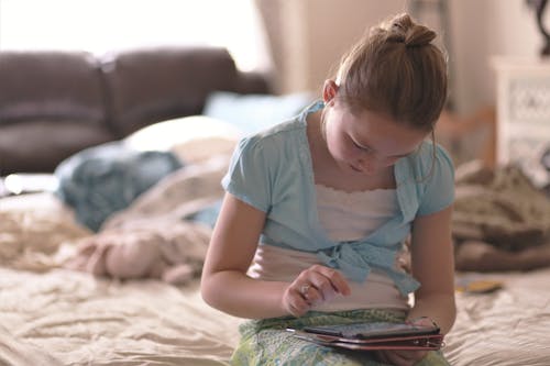 Free Girl Sitting on Bed Holding Tablet Computer Stock Photo