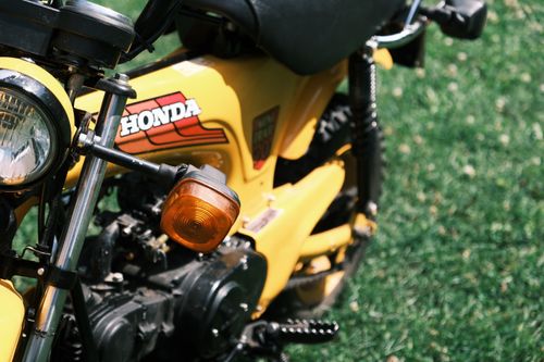 Free Close-up shot of a classic yellow Honda motorcycle with distinctive features in a grassy setting. Stock Photo