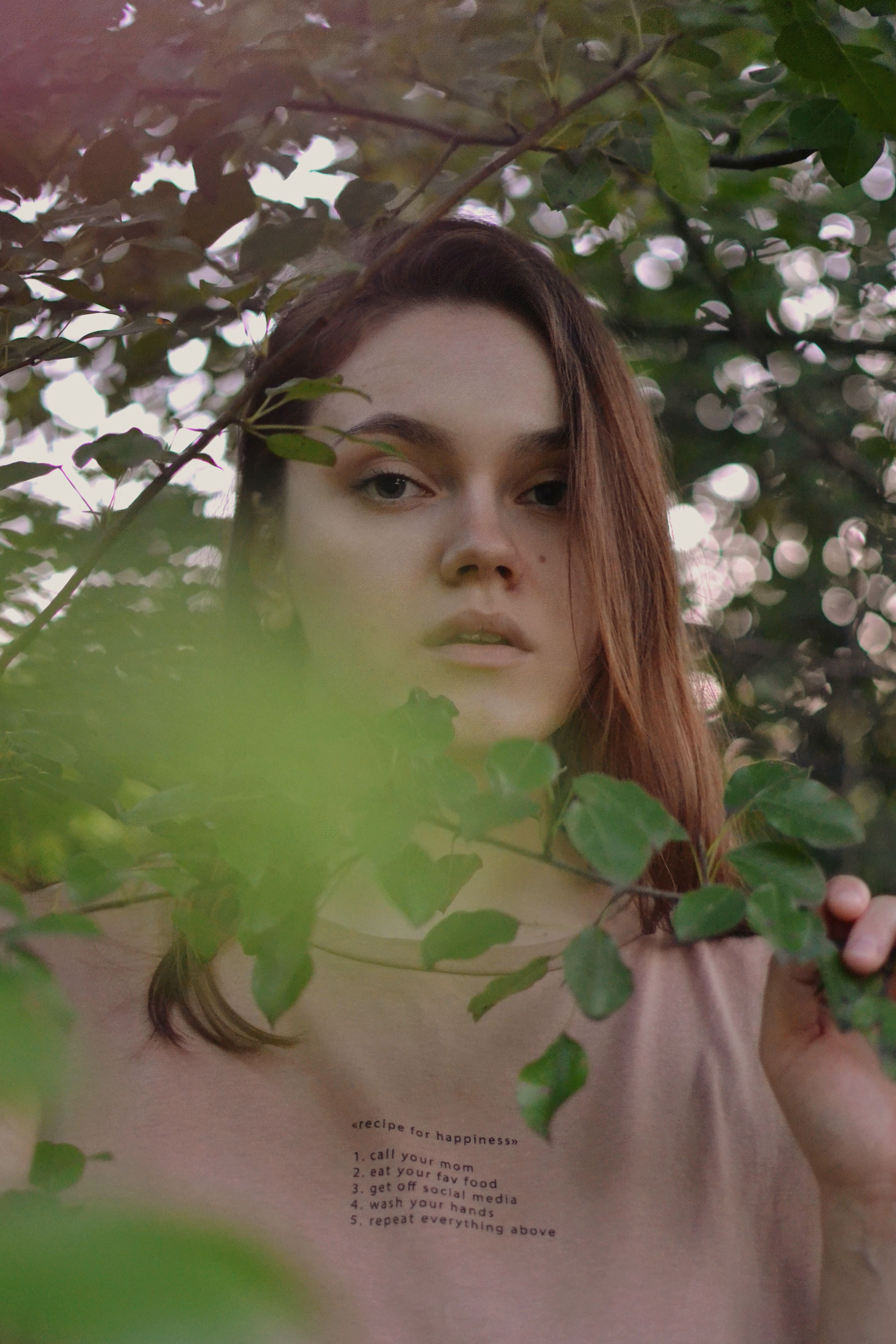 A serene portrait of a woman standing among lush green branches, capturing a tranquil moment.