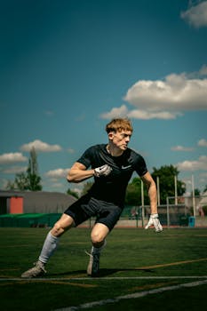 Focused athlete sprints on a soccer field wearing athletic gear. Captured under a clear blue sky.