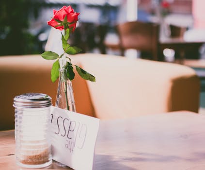 咖啡桌上放着一个花瓶，里面插着一朵鲜艳的红玫瑰，灯光柔和，装饰精美