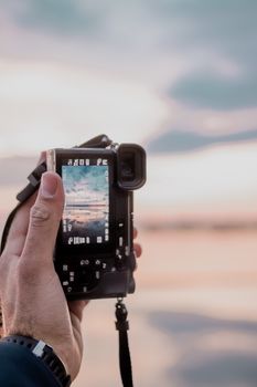Close-up of a hand holding a camera photographing a stunning landscape.