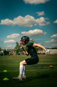 Athlete in football gear practicing on the field under a clear sky.