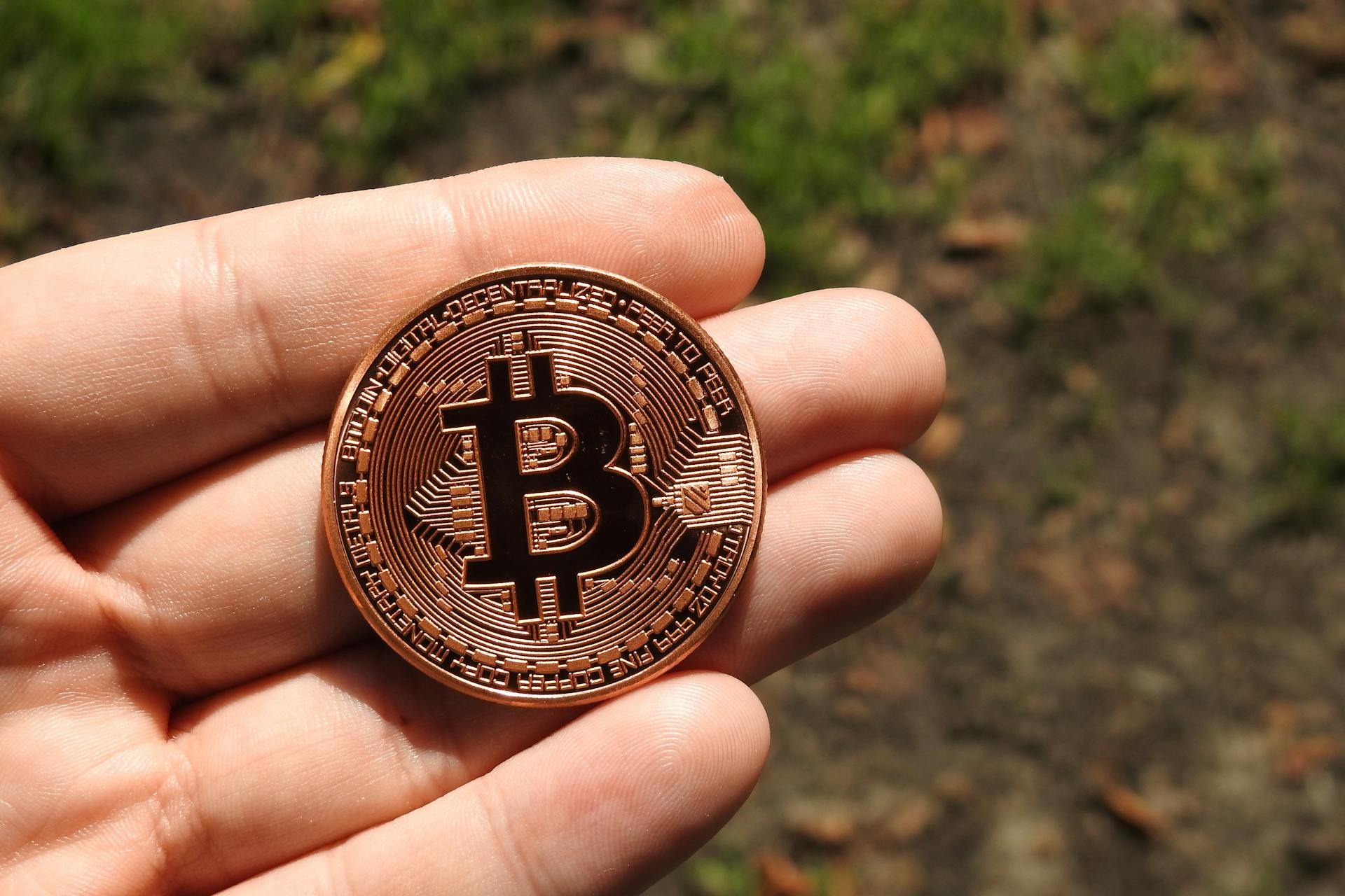 A close-up shot of a Bitcoin coin held in a person's hand outdoors, showcasing cryptocurrency's tangible side.