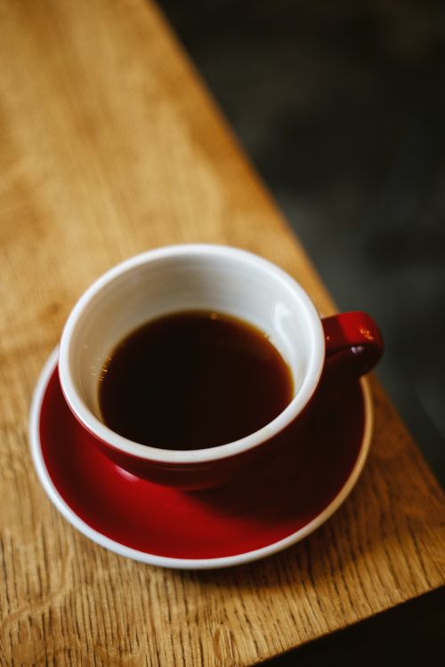 Free A steaming cup of black coffee in a vibrant red cup on a wooden table enhances its warmth. Stock Photo