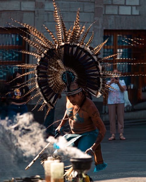 Man Wearing a Large Feather Plume Performing a Ritual with Smoke on a Street