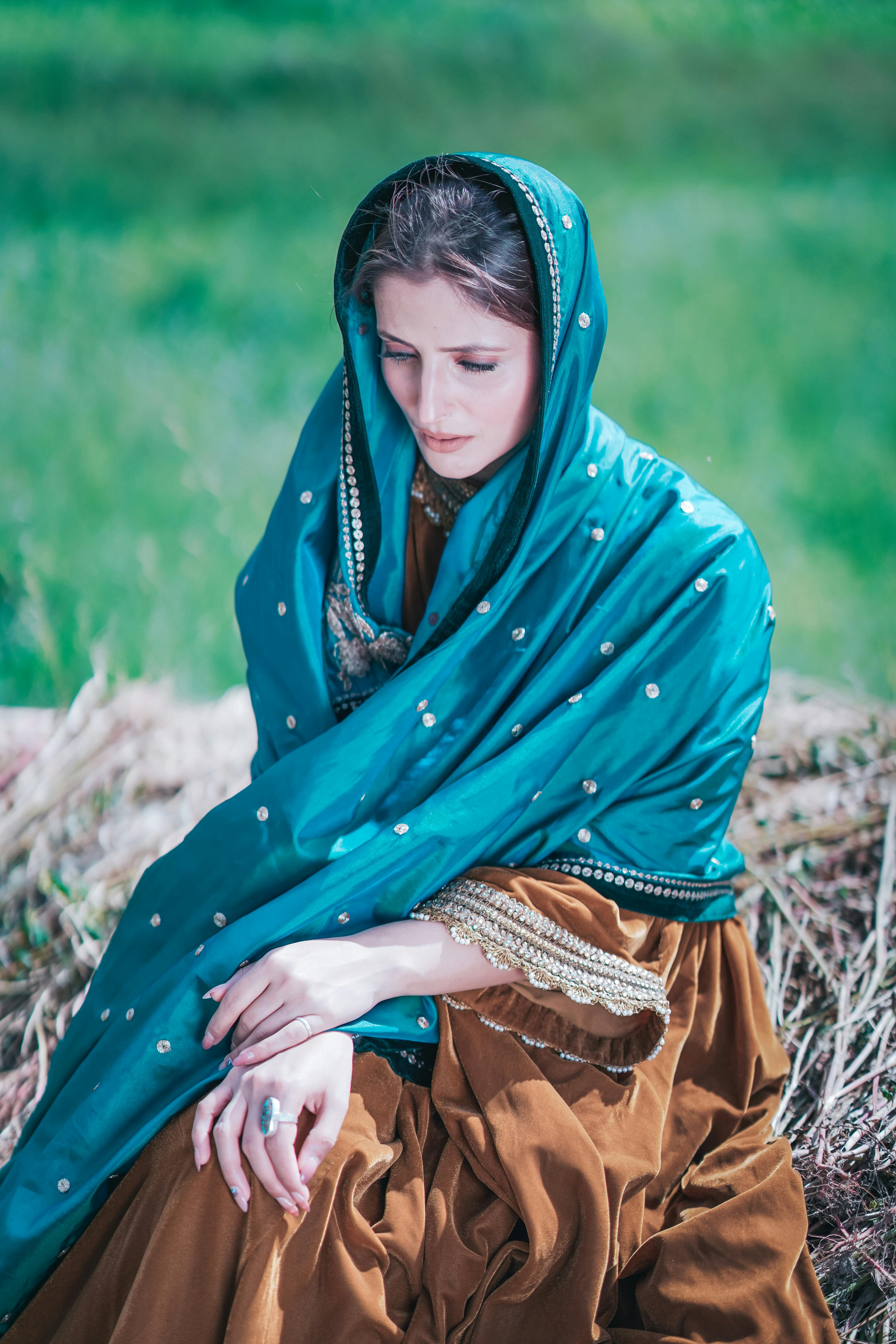 Beautiful woman in traditional dress with headscarf, sitting peacefully in nature.