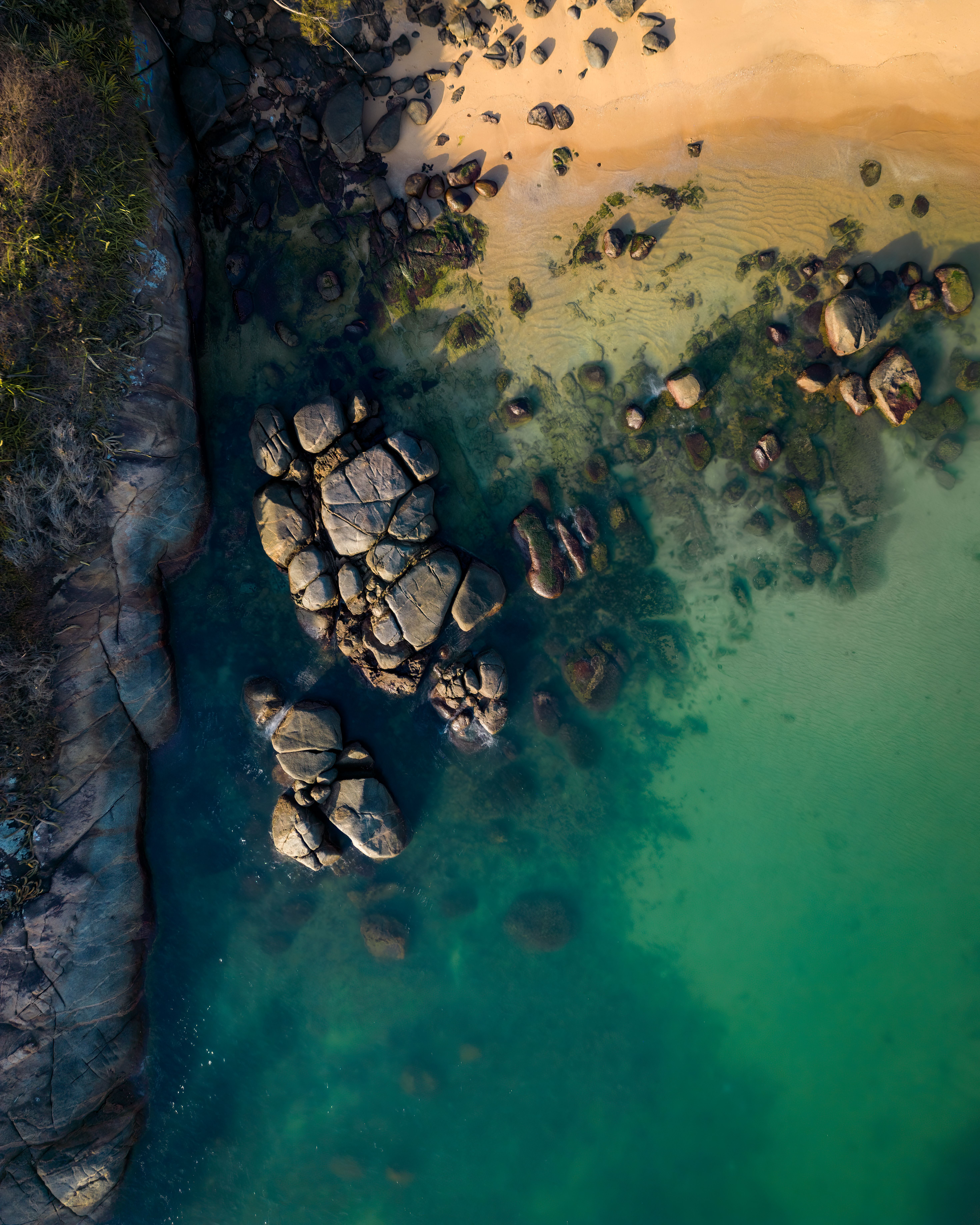 Drone shot of Praia da Costa's rocky shoreline with emerald waters, capturing vibrant nature.