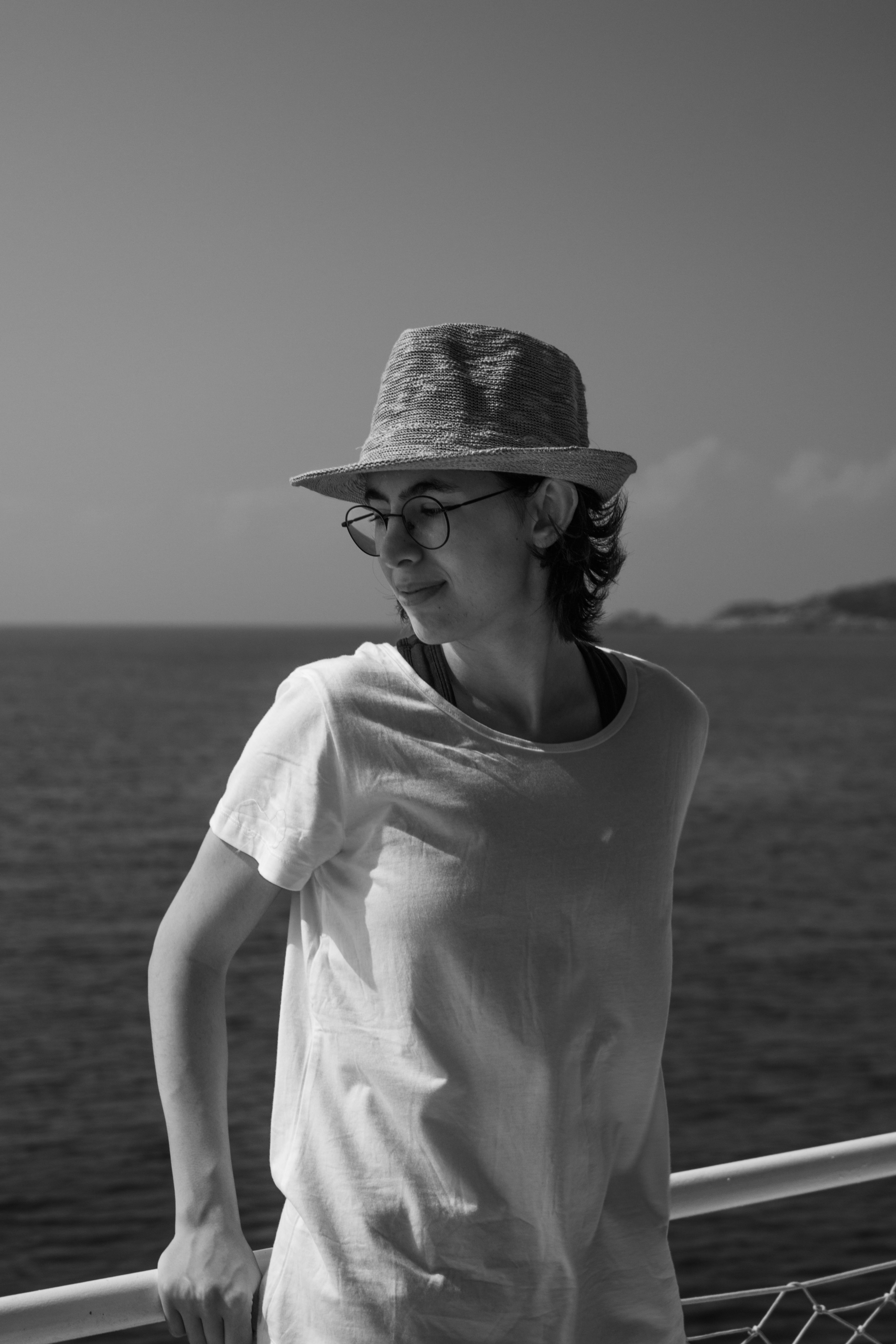 Black and white photo of a woman in a fedora, enjoying leisure time by the ocean.