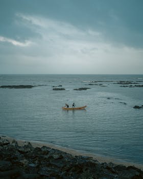 Two fishermen in a small boat on a calm sea near Mumbai, India against an overcast sky.