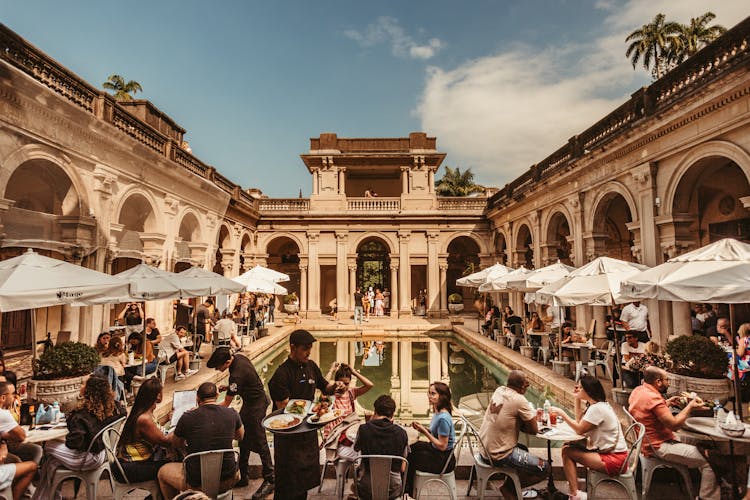 Symmetrical View Of A Palace Patio With A Pool, And People Dinning