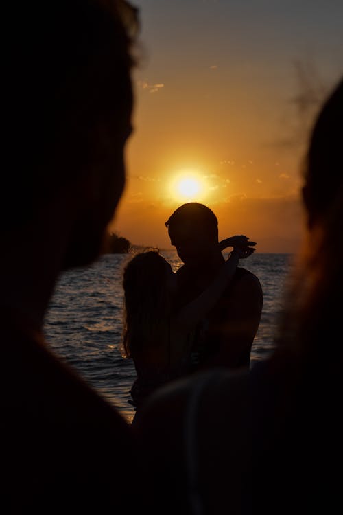 Silhouette of People Sitting on Seashore during Sunset