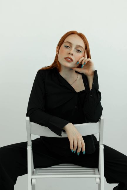 Studio shot of a young redheaded woman sitting on a chair, exuding elegance and confidence.