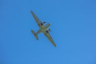 A classic Douglas DC-3 airplane flying above with a clear blue sky backdrop.