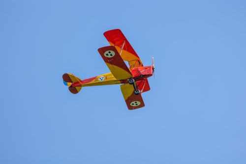 Free A vivid red and yellow vintage biplane flying against a clear blue sky, perfectly capturing aviation history. Stock Photo