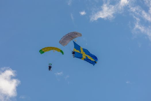 Parachutists skydiving with a Swedish flag against a clear blue sky, showcasing adventure and freedom.