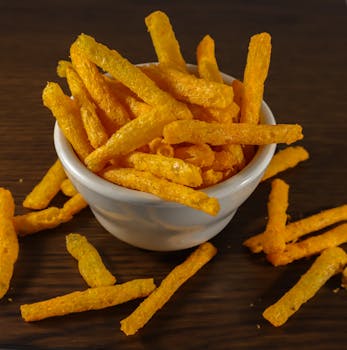 Close-up of crispy cheese sticks in a white bowl on a wooden table, perfect for snack time.