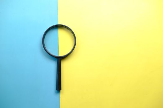 A magnifying glass lays on a split blue and yellow background in a flat lay style.