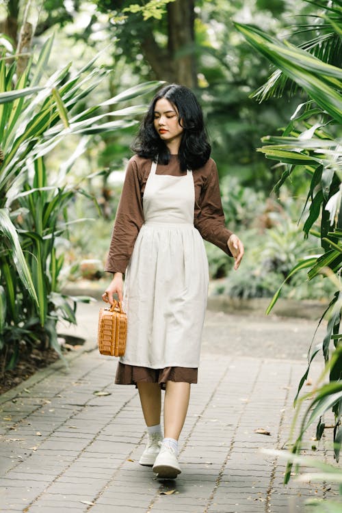 Woman in Brown Long Sleeve Dress with White Apron Holding Woven Basket