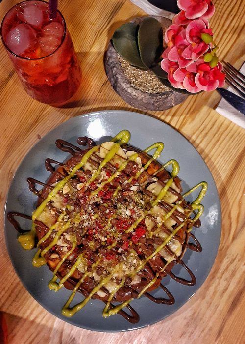 Free A top view of a Waffle dessert garnished with nuts, chocolate drizzles, and fruit, paired with a refreshing iced drink. Stock Photo