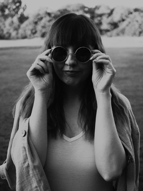 Free Black and white portrait of a woman adjusting sunglasses in a park setting. Stock Photo