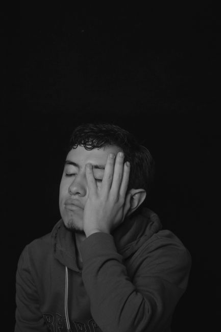 Fotomural Una imagen en escala de grises que muestra a un hombre cansado con la mano en la cara, vistiendo una sudadera.