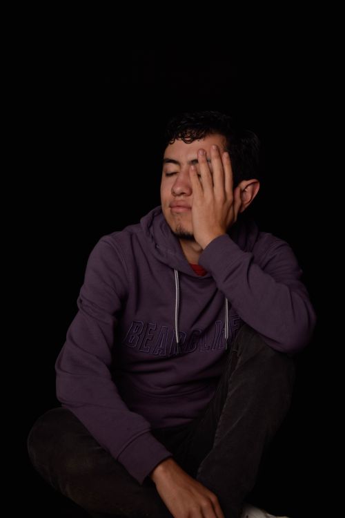 Free Portrait of a young man in a purple hoodie sitting with his eyes closed against a black background. Stock Photo