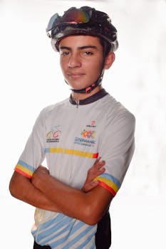 Young male cyclist wearing a helmet and jersey, posing confidently with arms crossed.