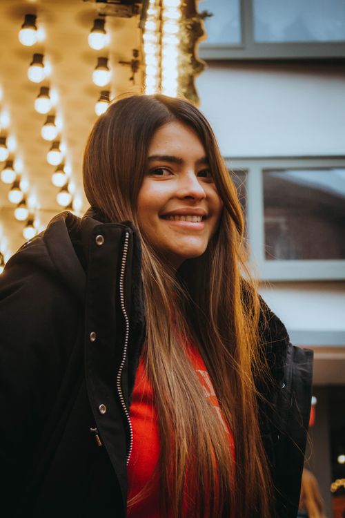 Free A woman smiles warmly in an urban environment with decorative lights. Stock Photo