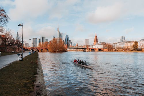 People Paddling while Riding a Boat on the River Near City Buildings