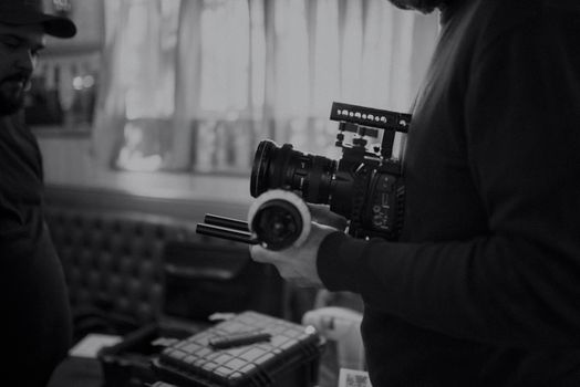 Grayscale photo of a filmmaker holding professional camera indoors.
