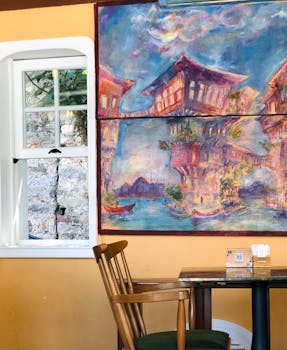 Inviting cafe interior featuring a bold, colorful painting beside a bright window, with wooden chair and table.