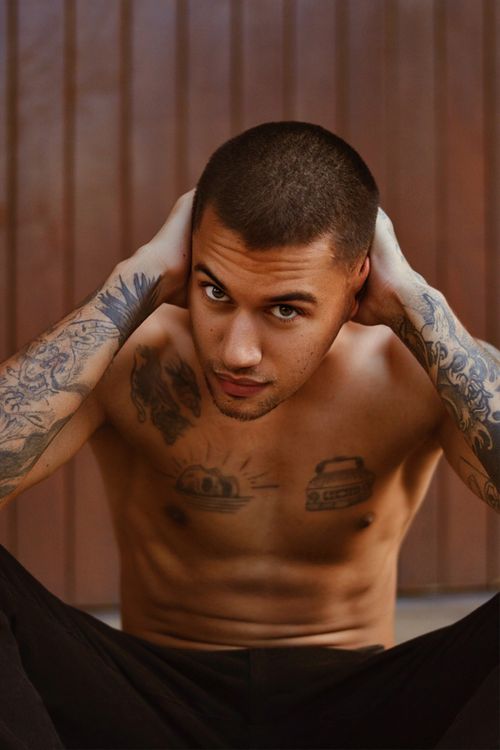Free Shirtless man with tattoos poses confidently against a wooden backdrop in Sete Lagoas, Brazil. Stock Photo