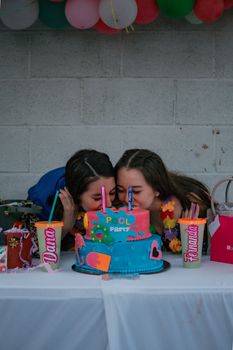 Two young women enjoying a birthday celebration with a pool-themed cake and festive decor.